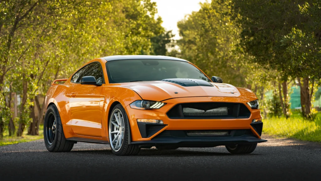 A sleek orange sports car parked on a scenic outdoor path surrounded by lush greenery
