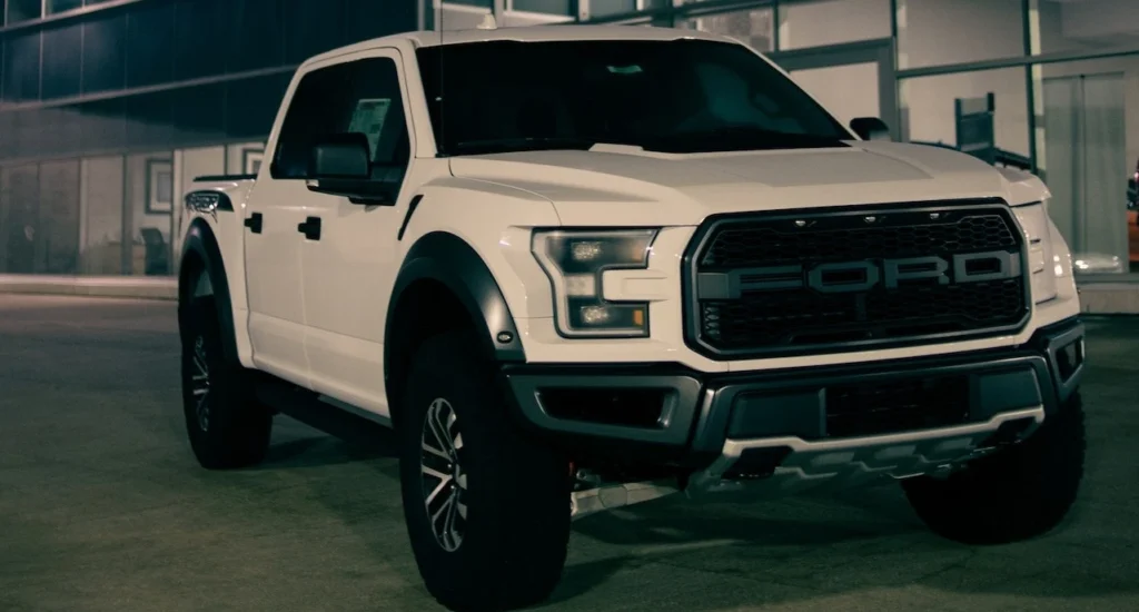 White pickup truck parked outside a Ford dealership at night, showcasing its luxury and modern design