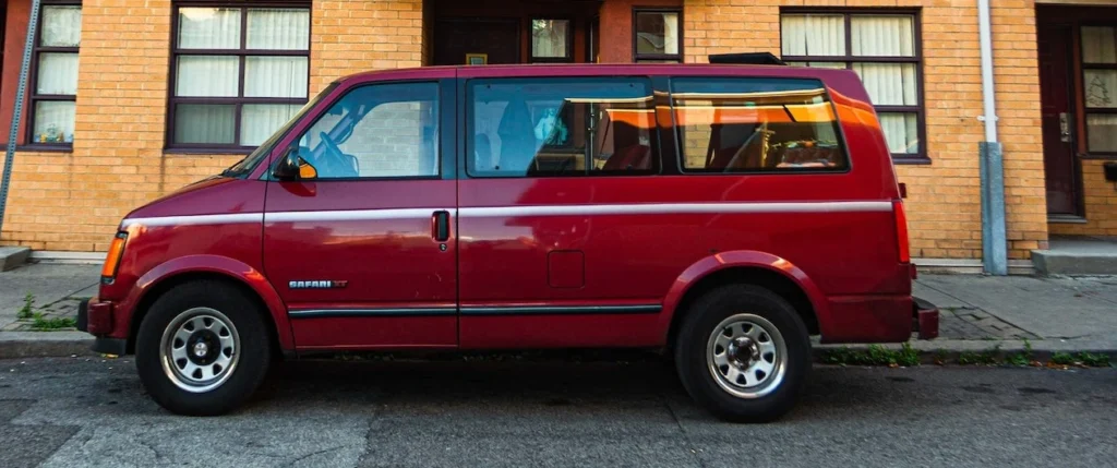 A vibrant red van parked curbside in front of a colorful urban apartment building