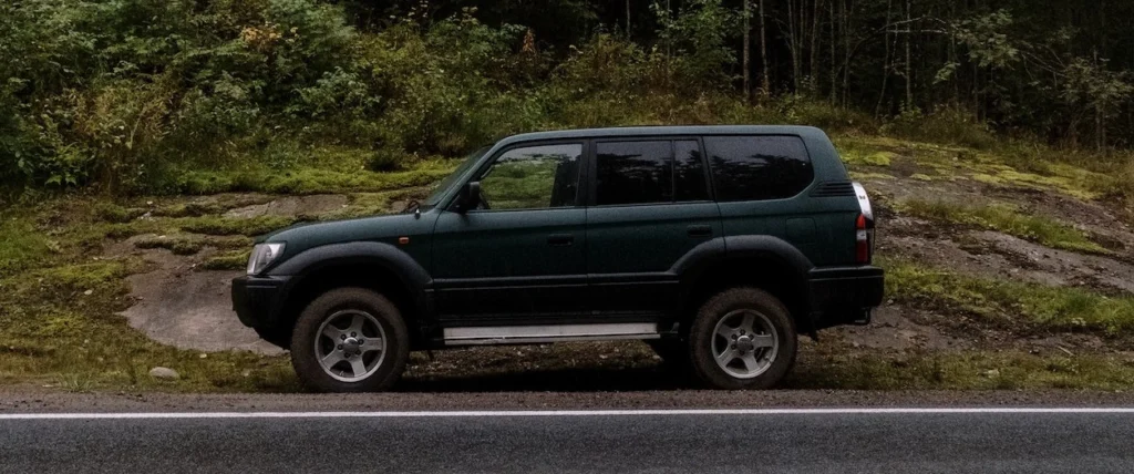 A lone SUV parked on a forest-lined roadside, perfect for travel themes