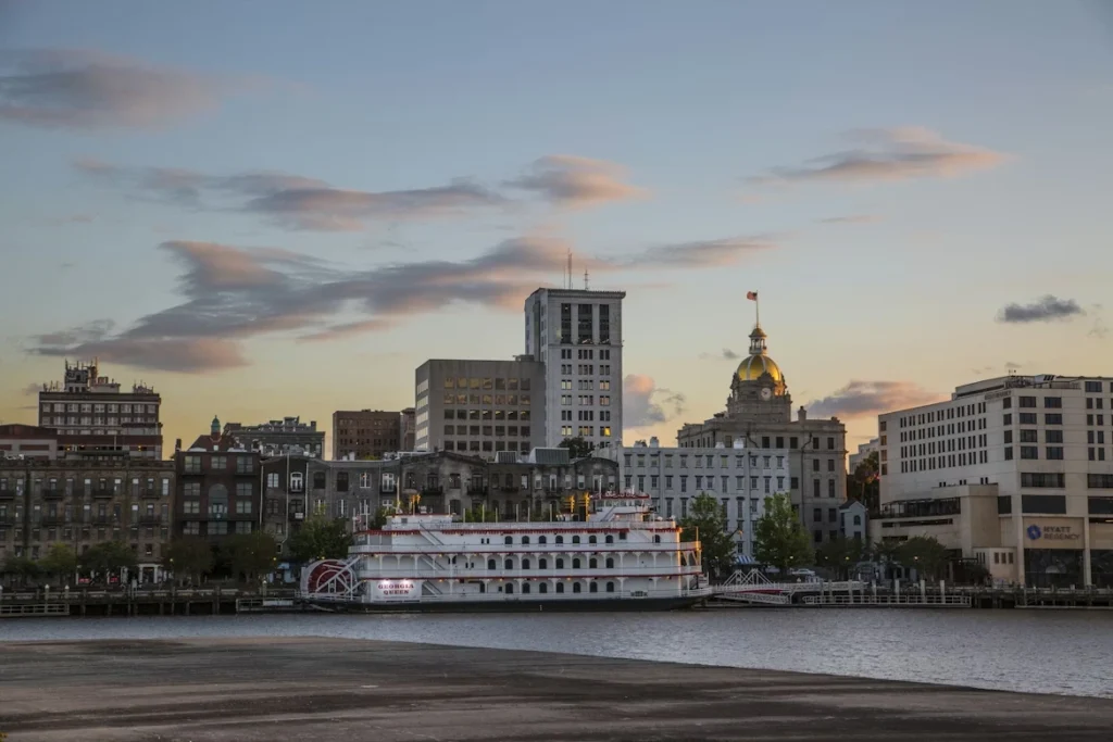 White and brown boat on sea near city buildings during sunset, in Savannah, Georgia