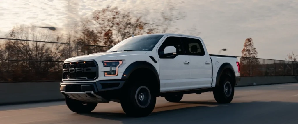 White pickup truck speeding along a highway under a cloudy sky
