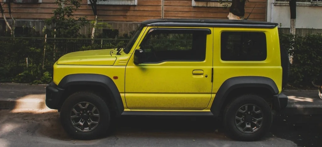 A vibrant yellow SUV parked beside a residential building amidst trees on a city street