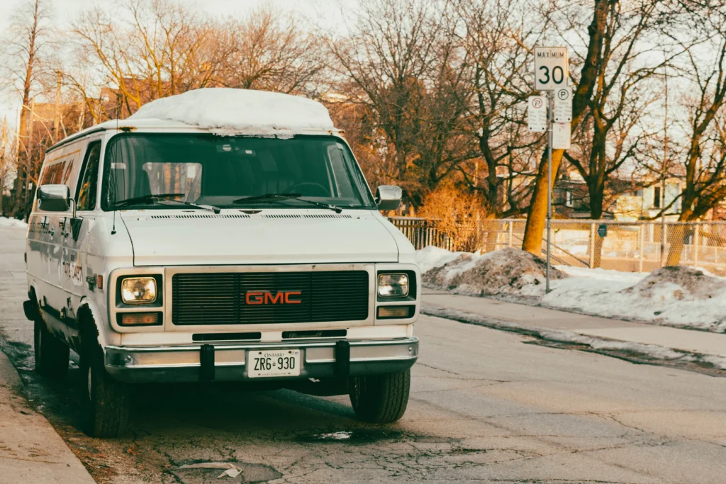 Vintage GMC van covered with snow parked on a snowy street intersection with winter trees around