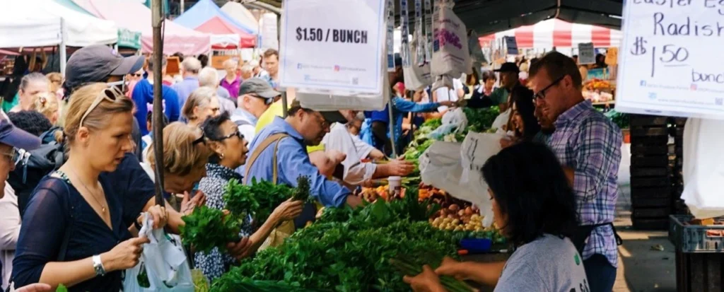 Lively city market scene with people buying fresh vegetables at outdoor stalls