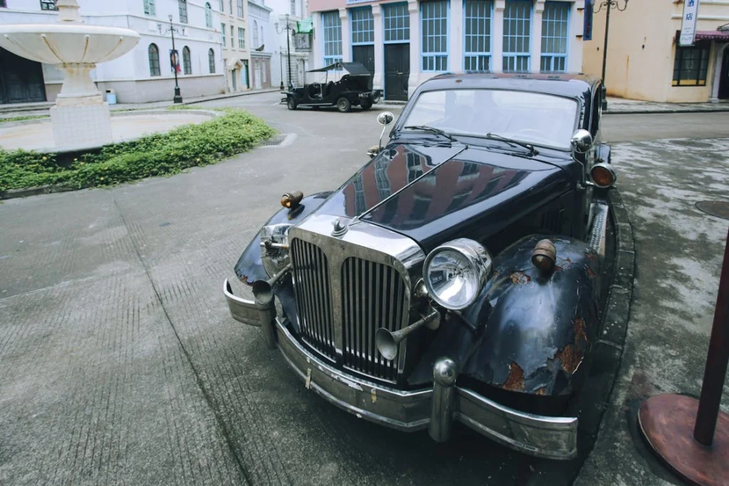 A classic rusty car sits parked on a quiet urban street corner with an old world charm