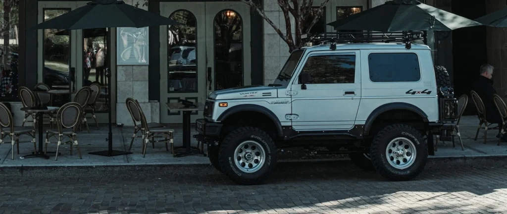 A white SUV parked in front of a café in an urban area with trees